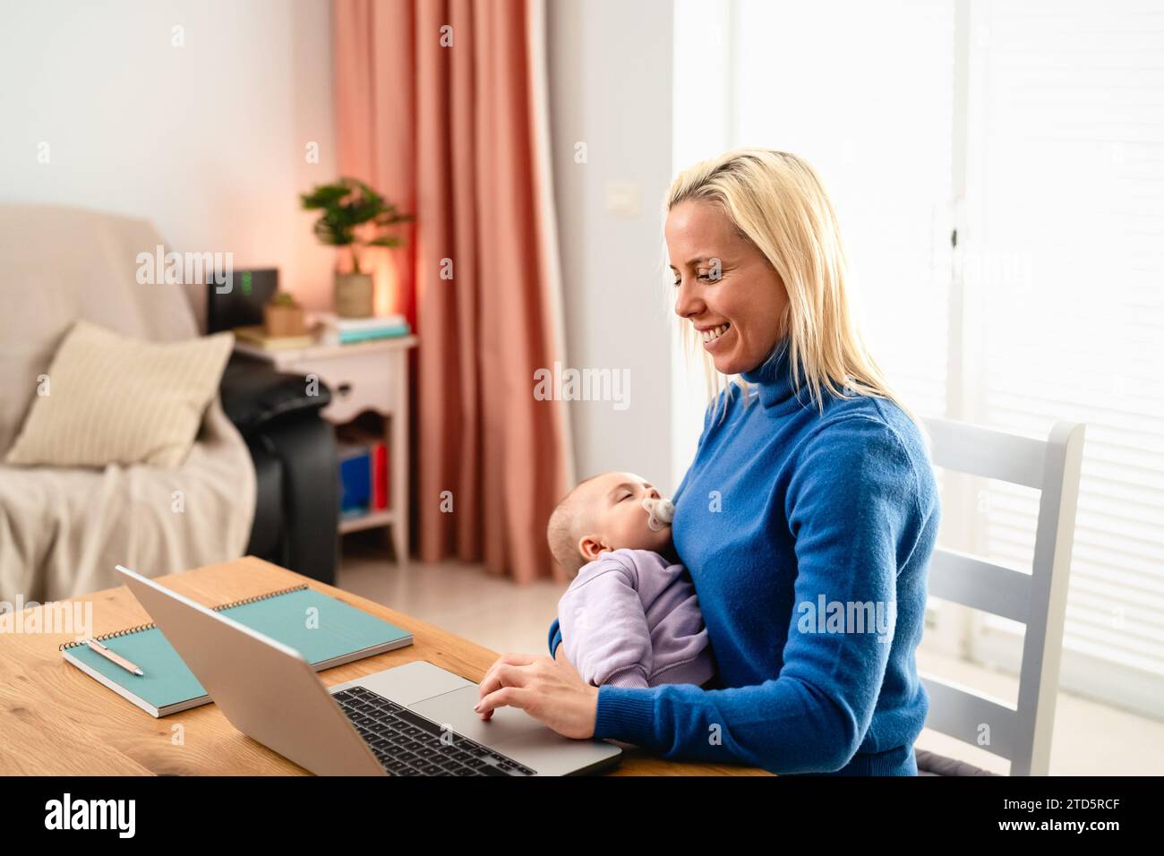 Mamma felice che usa il laptop mentre il suo bambino sta dormendo Foto Stock