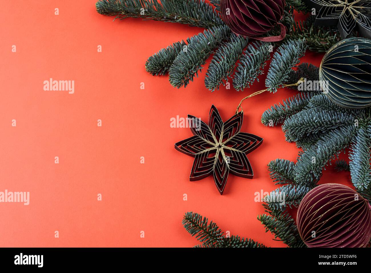 Fiocco di neve giocattolo di carta a nido d'ape su sfondo rosso. Rami di abete e balli di Natale, concetto di Capodanno. Vista dall'alto, base piatta, spazio di copia. Foto Stock