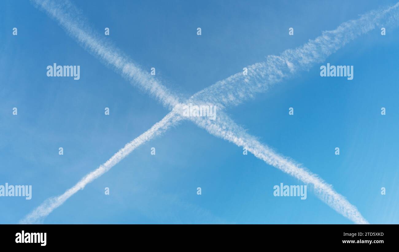 Aeromobile contrails crossing e formando una X in un cielo blu Foto Stock