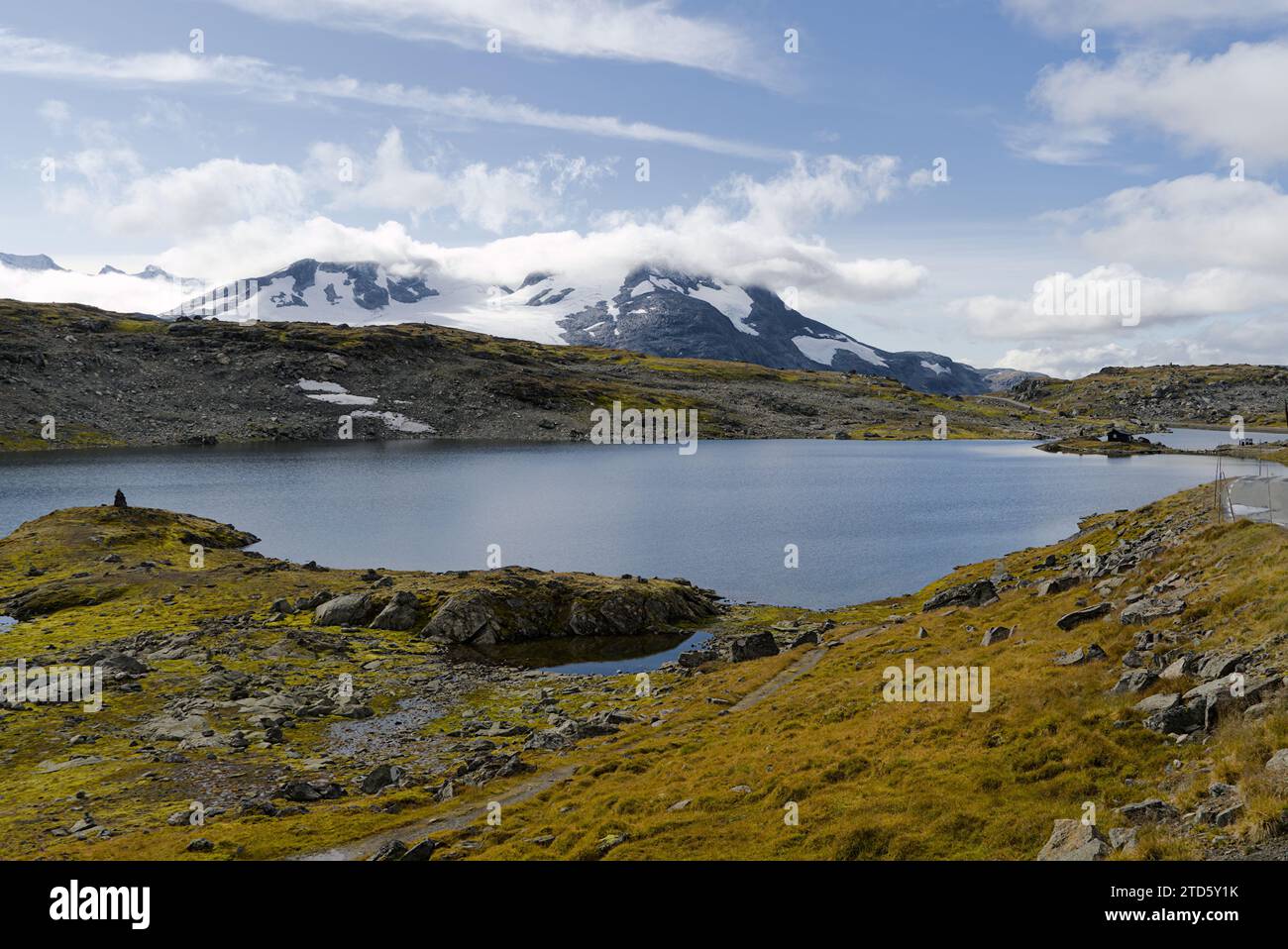 Il lago è circondato da montagne coperte di neve sotto il cielo blu con alcune nuvole bianche in Norvegia. Foto Stock