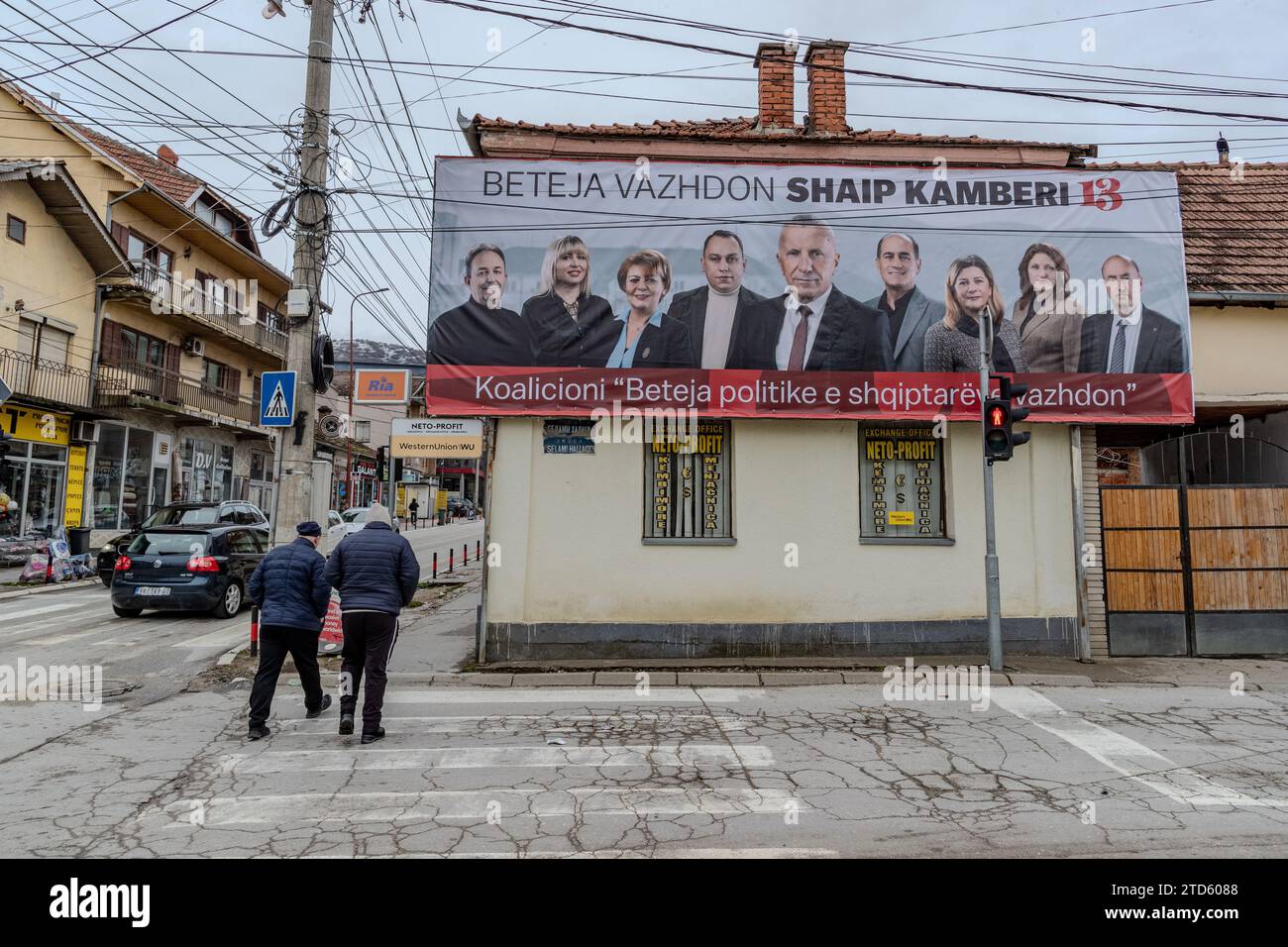 Preshevo, Repiblic di Serbia. 16 dicembre 2023. A Preshevo i pedoni passano un poster della campagna elettorale di Shaip Kamberi, un albanese che si candida per la rielezione come deputato all'Assemblea serba con una coalizione a cinque partiti. Questa scena mette in luce le preoccupazioni della comunità albanese circa il crescente potere di Aleksandar Vucic e le sue implicazioni per la loro sicurezza e posizione in Serbia. (VX Photo/ Vudi Xhymshiti) credito: VX Pictures/Alamy Live News Foto Stock