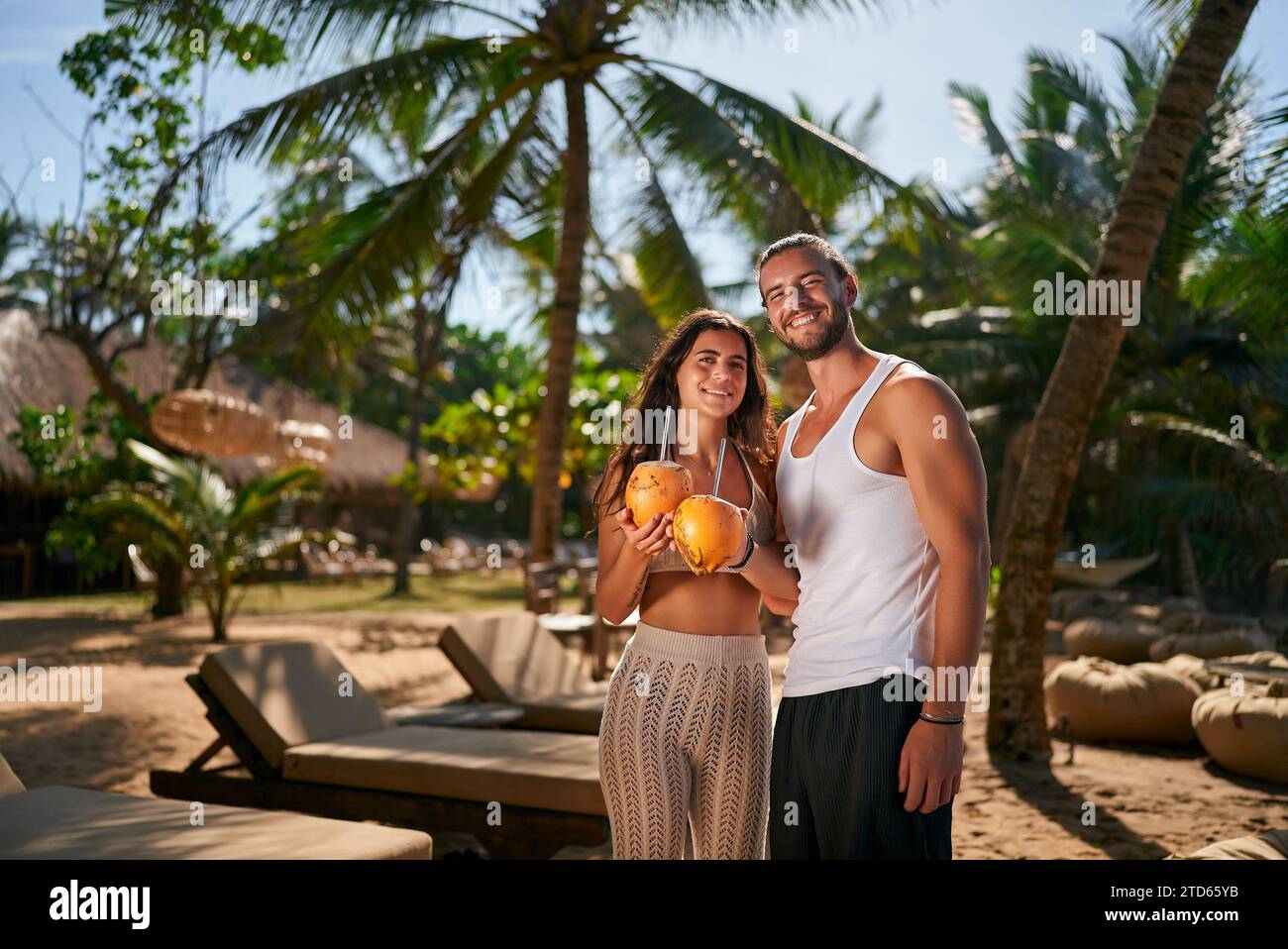 La coppia felice ama il resort tropicale, l'uomo e la donna tengono una bevanda al cocco. Romantica vacanza di nozze, relax sulla spiaggia, amore. Sorriso duo baciato dal sole Foto Stock