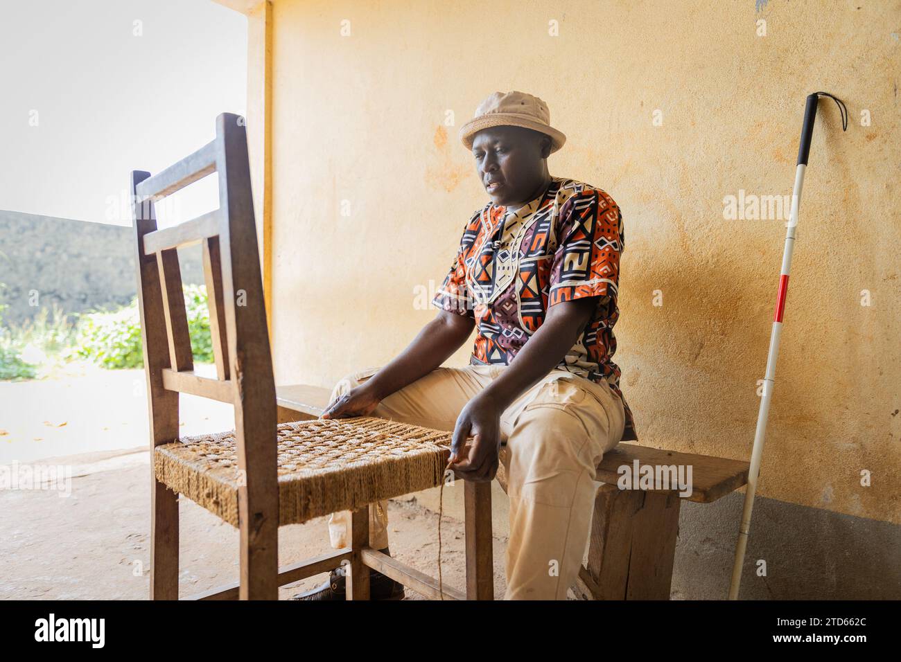 Uomo africano cieco impegnato a finire tessendo sedie da pranzo. Cecità e lavoro a mano concetto. Foto Stock