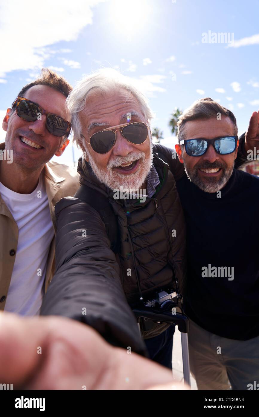 Allegro gruppo di uomini caucasici di mezza età che indossano occhiali da sole che scattano un selfie con un cellulare. Foto Stock
