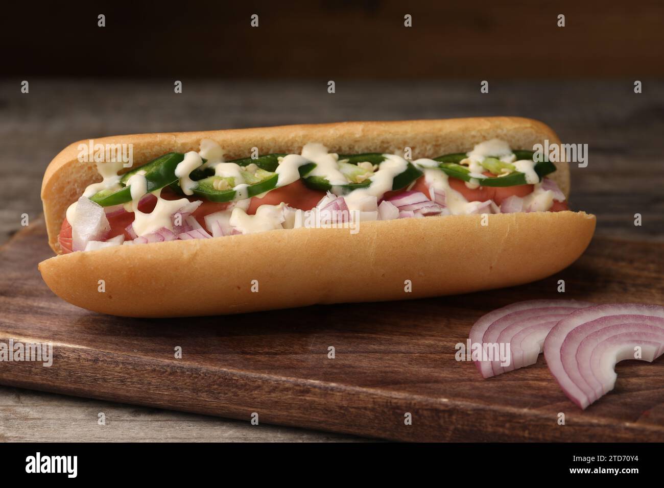 Delizioso hot dog con cipolla, peperoncino e salsa su un tavolo di legno, primo piano Foto Stock