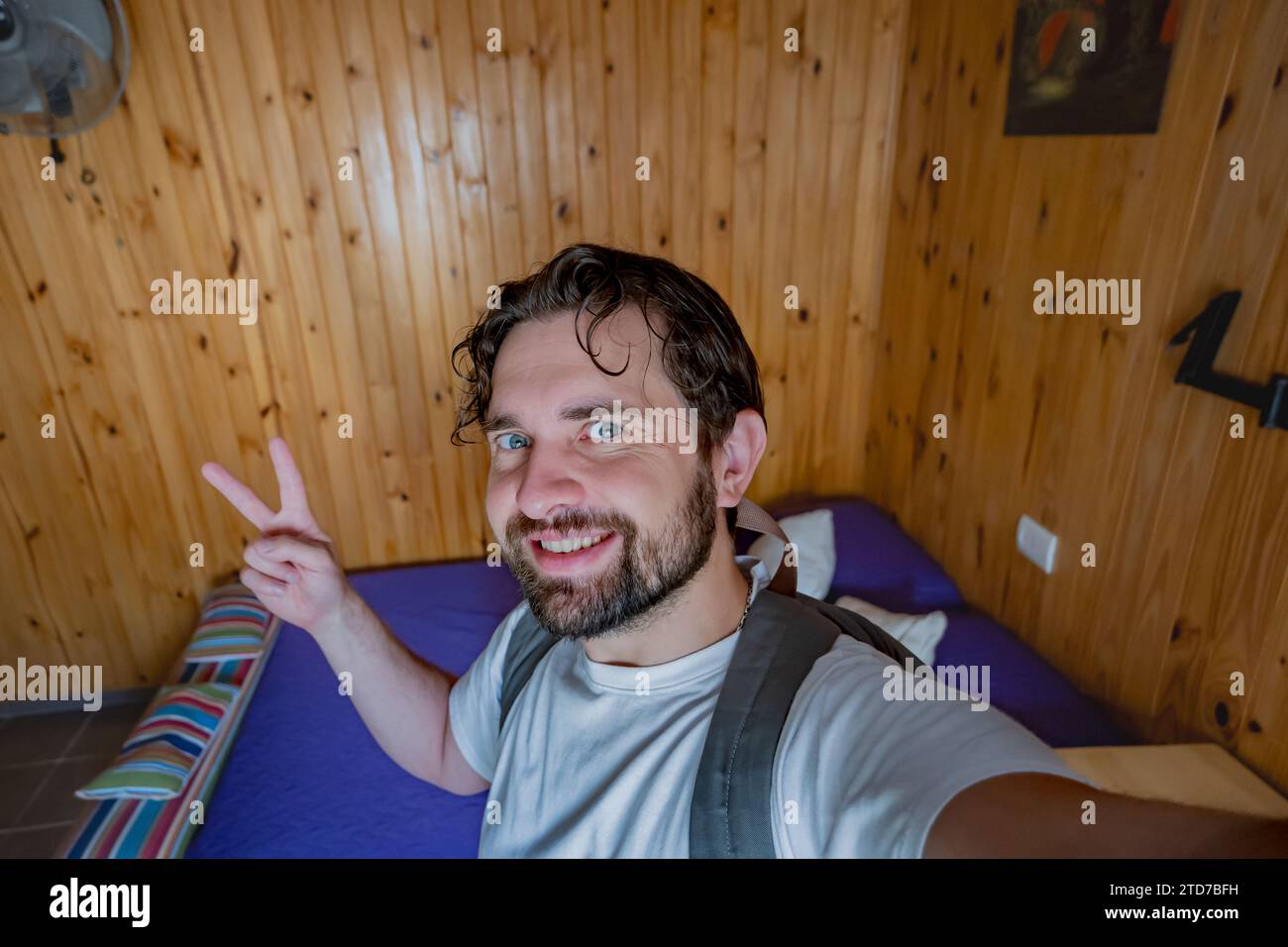 Un turista che scatta un selfie all'interno di una stanza in affitto. Fa il segno di pace con le mani. Foto Stock