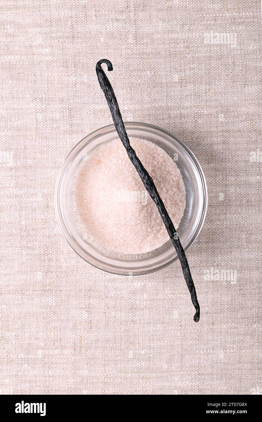 Fagioli di vaniglia e zucchero di vaniglia, in recipiente di vetro, su lino. Frutto secco, intero, marrone, maturo di Vanilla planifolia. Spezie dal sapore inconfondibile. Foto Stock