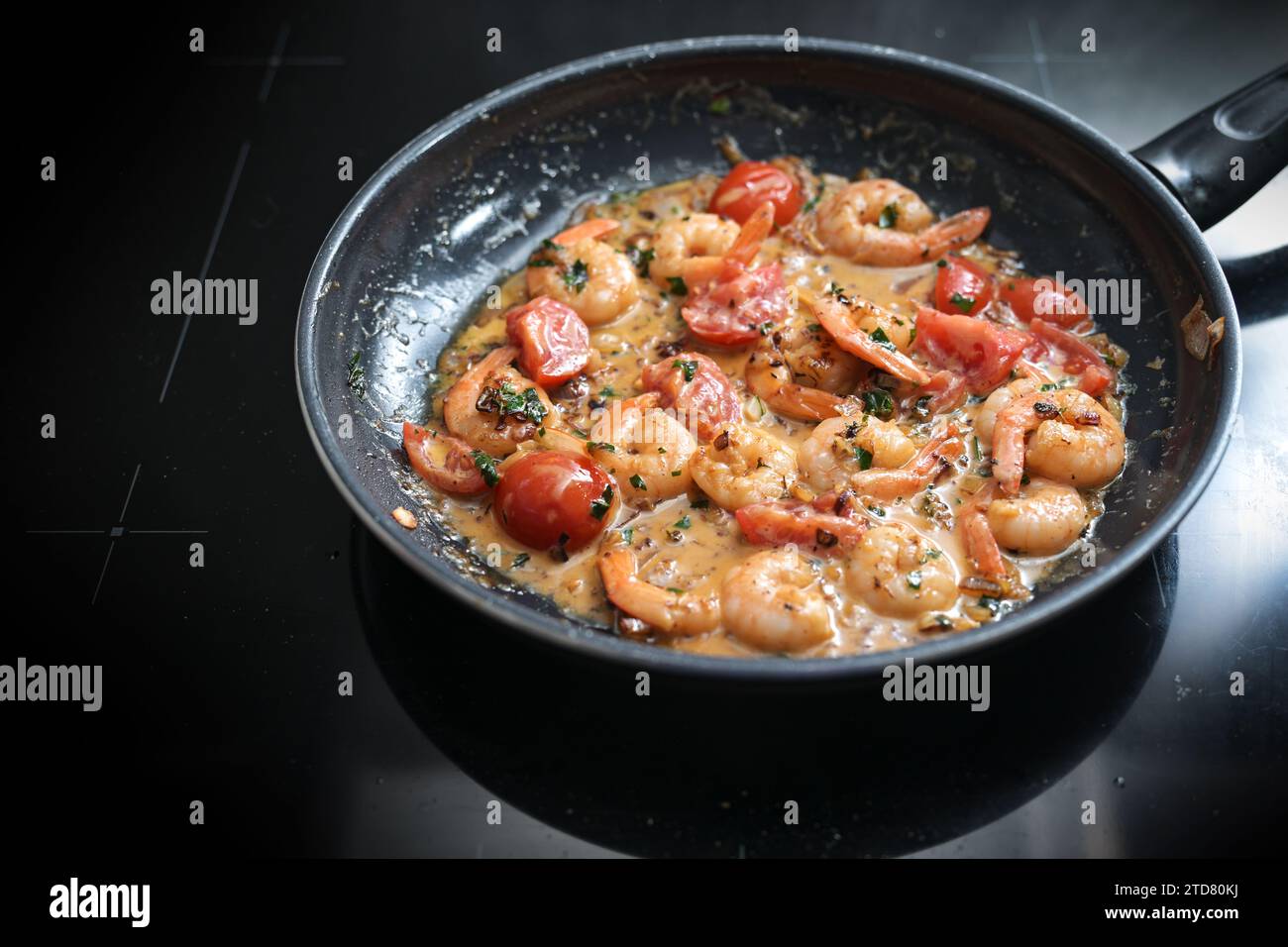 Gamberetti in salsa di pomodoro saltati con erbe, cipolle e aglio in una padella nera sul piano cottura, cucinando un pasto mediterraneo a base di pesce, sele Foto Stock