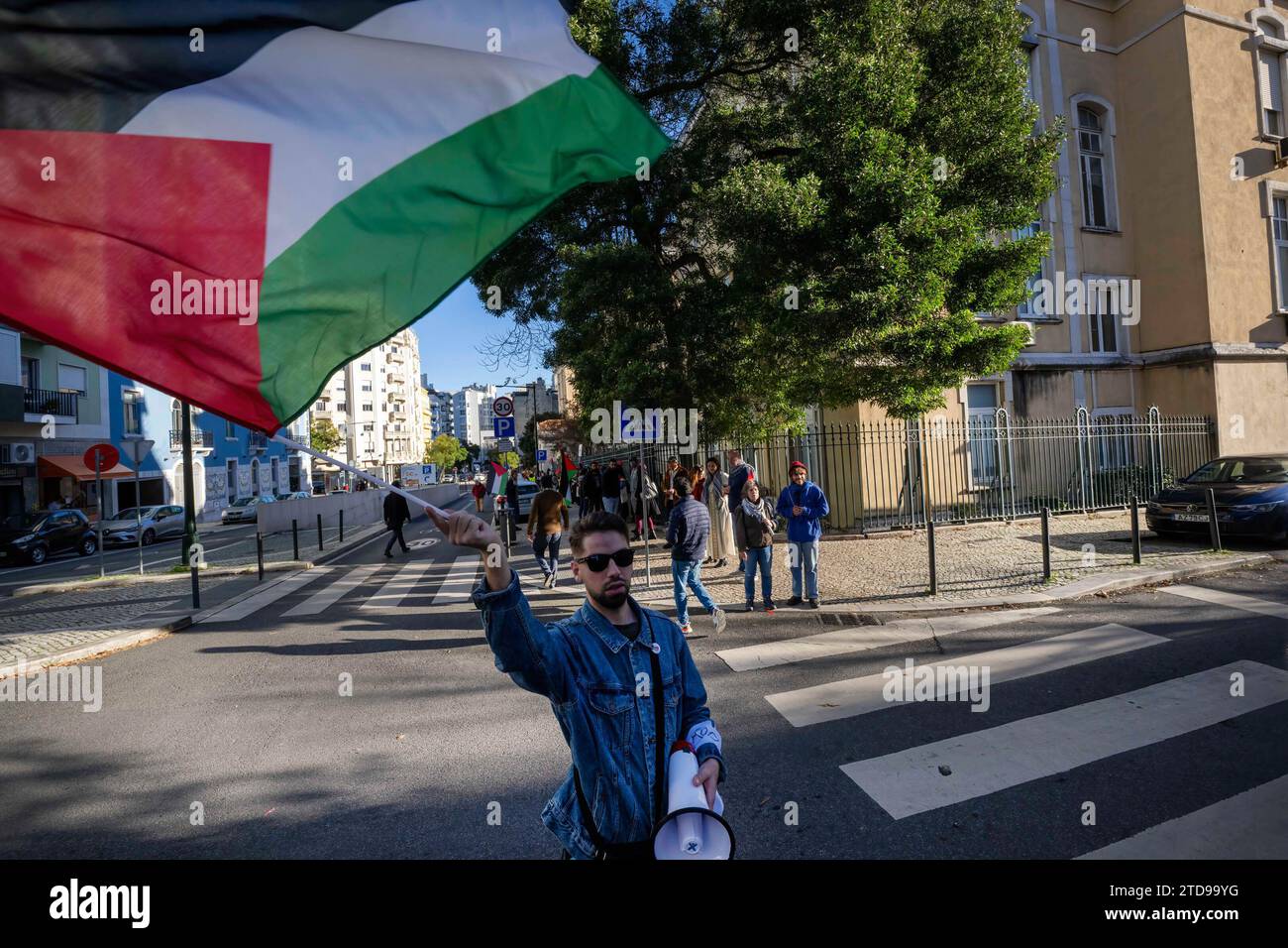 Lisbona, Portogallo. 16 dicembre 2023. Un attivista sventola una bandiera palestinese durante una manifestazione vicino all'ambasciata israeliana. Le azioni di protesta sono state organizzate dal PUSP - Plataforma Unitária de Solidariedade com a Palestina, il che richiede al governo israeliano un cessate il fuoco immediato e permanente, la fine dell'assedio e l'ingresso illimitato di aiuti umanitari nella Striscia di Gaza, nonché la fine dell'aggressione nelle città, nei villaggi e nei campi profughi di tutta la Palestina. Credito: SOPA Images Limited/Alamy Live News Foto Stock