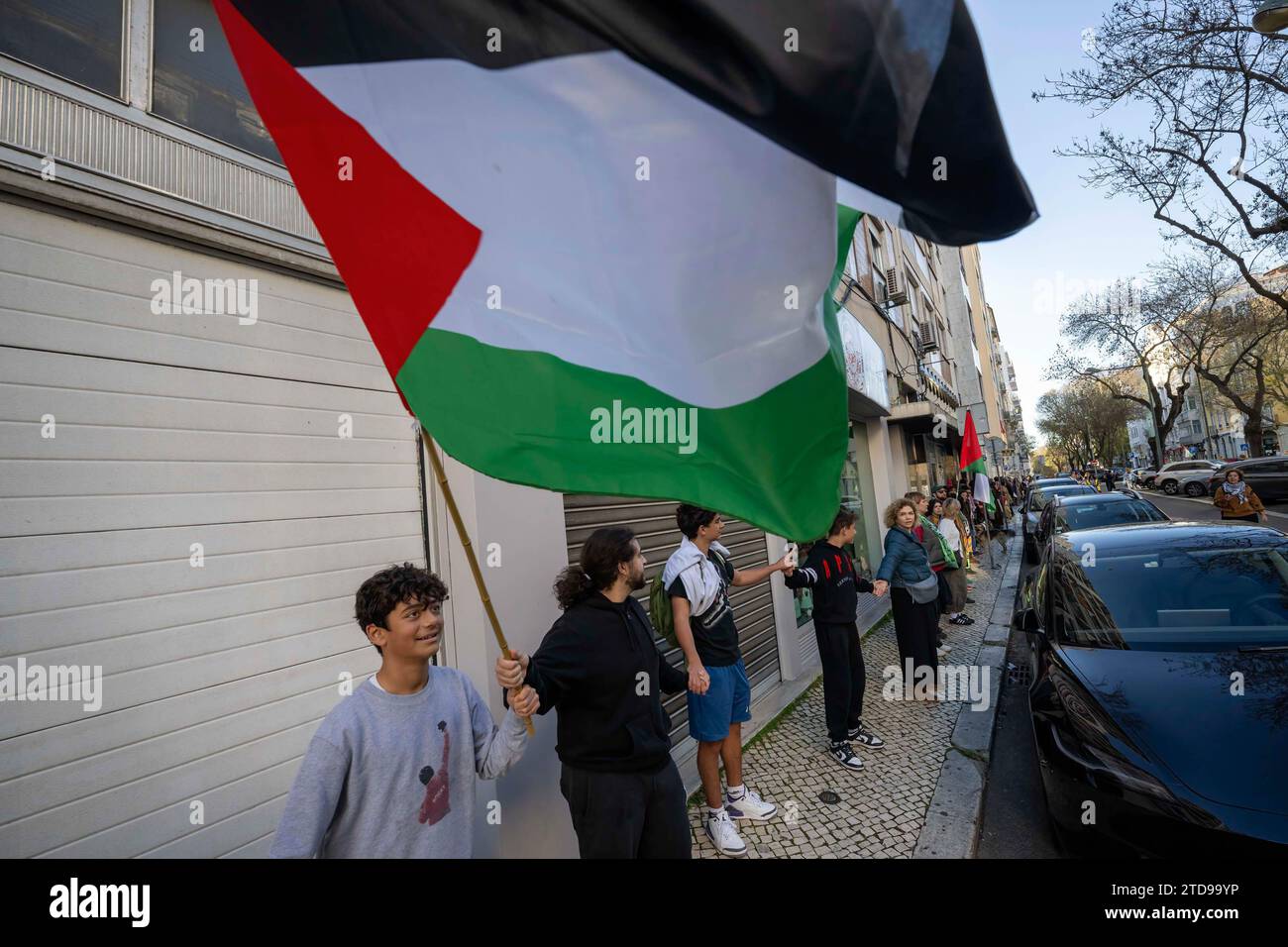 Lisbona, Portogallo. 16 dicembre 2023. Un attivista tiene una manifestazione di bandiera palestinese vicino all'ambasciata israeliana. Le azioni di protesta sono state organizzate dal PUSP - Plataforma Unitária de Solidariedade com a Palestina, il che richiede al governo israeliano un cessate il fuoco immediato e permanente, la fine dell'assedio e l'ingresso illimitato di aiuti umanitari nella Striscia di Gaza, nonché la fine dell'aggressione nelle città, nei villaggi e nei campi profughi di tutta la Palestina. Credito: SOPA Images Limited/Alamy Live News Foto Stock