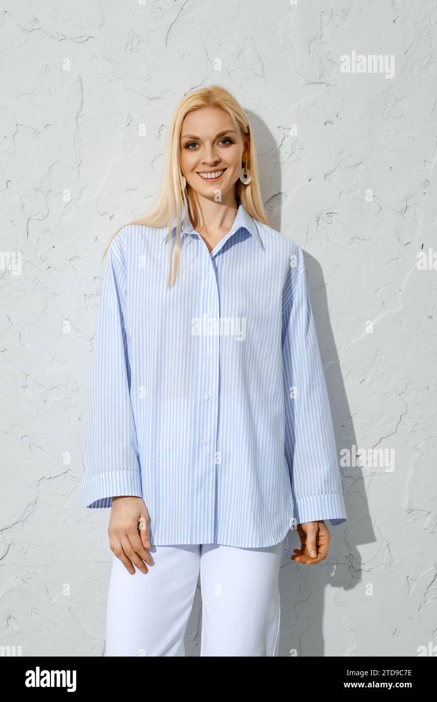 Comodo outfit estivo. Donna sorridente in camicetta di cotone blu accanto alla parete bianca Foto Stock