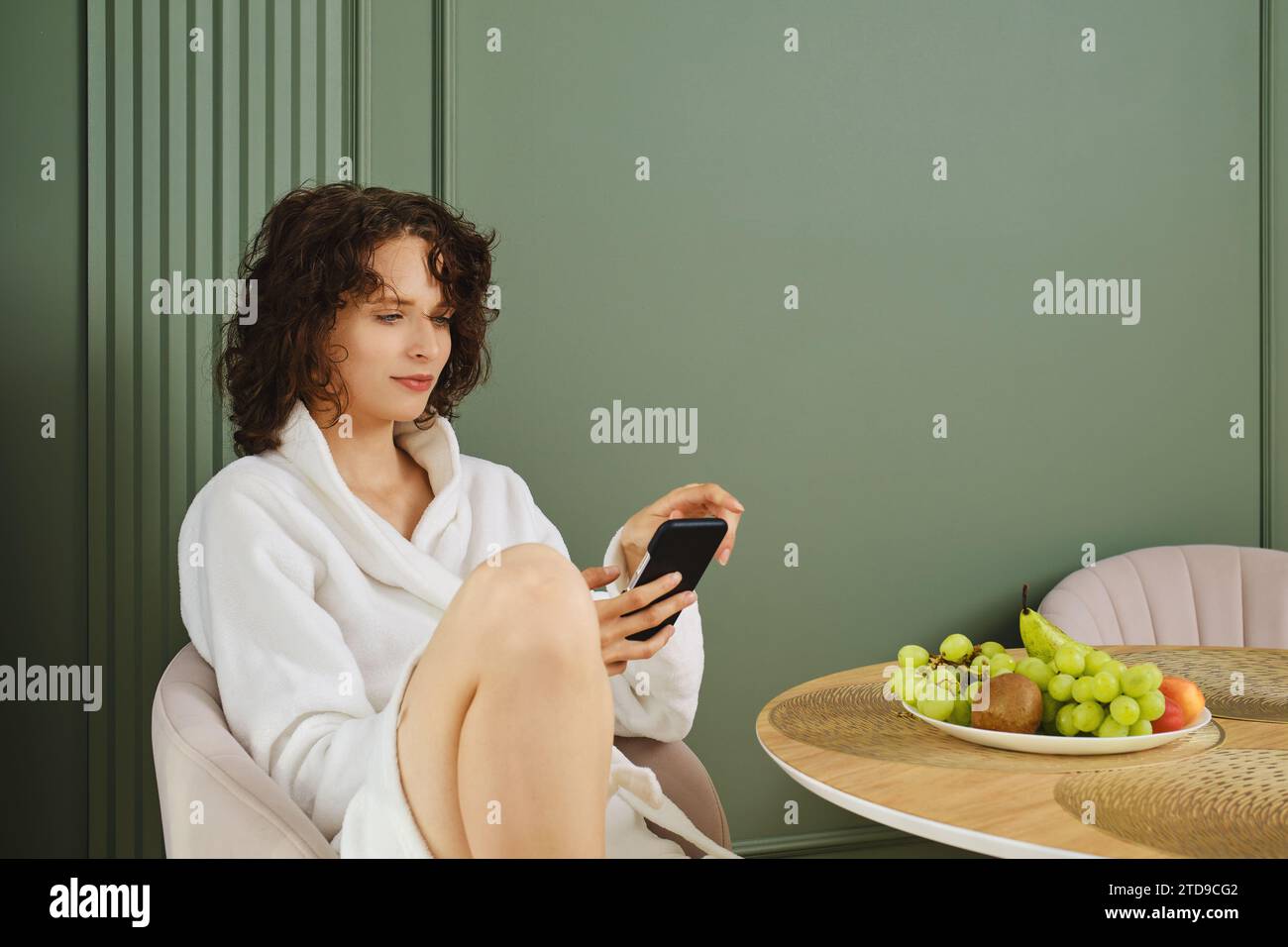 Una giovane donna che compone il numero della sua amica mentre è seduta al tavolo dopo la doccia Foto Stock