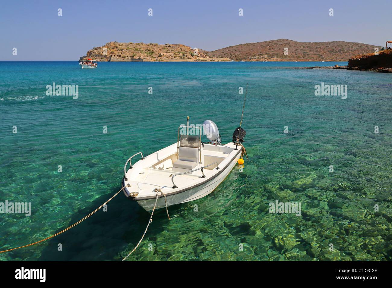 Piccola barca in primo piano con l'isola di spinalonga in lontananza nel mare turchese. Foto Stock