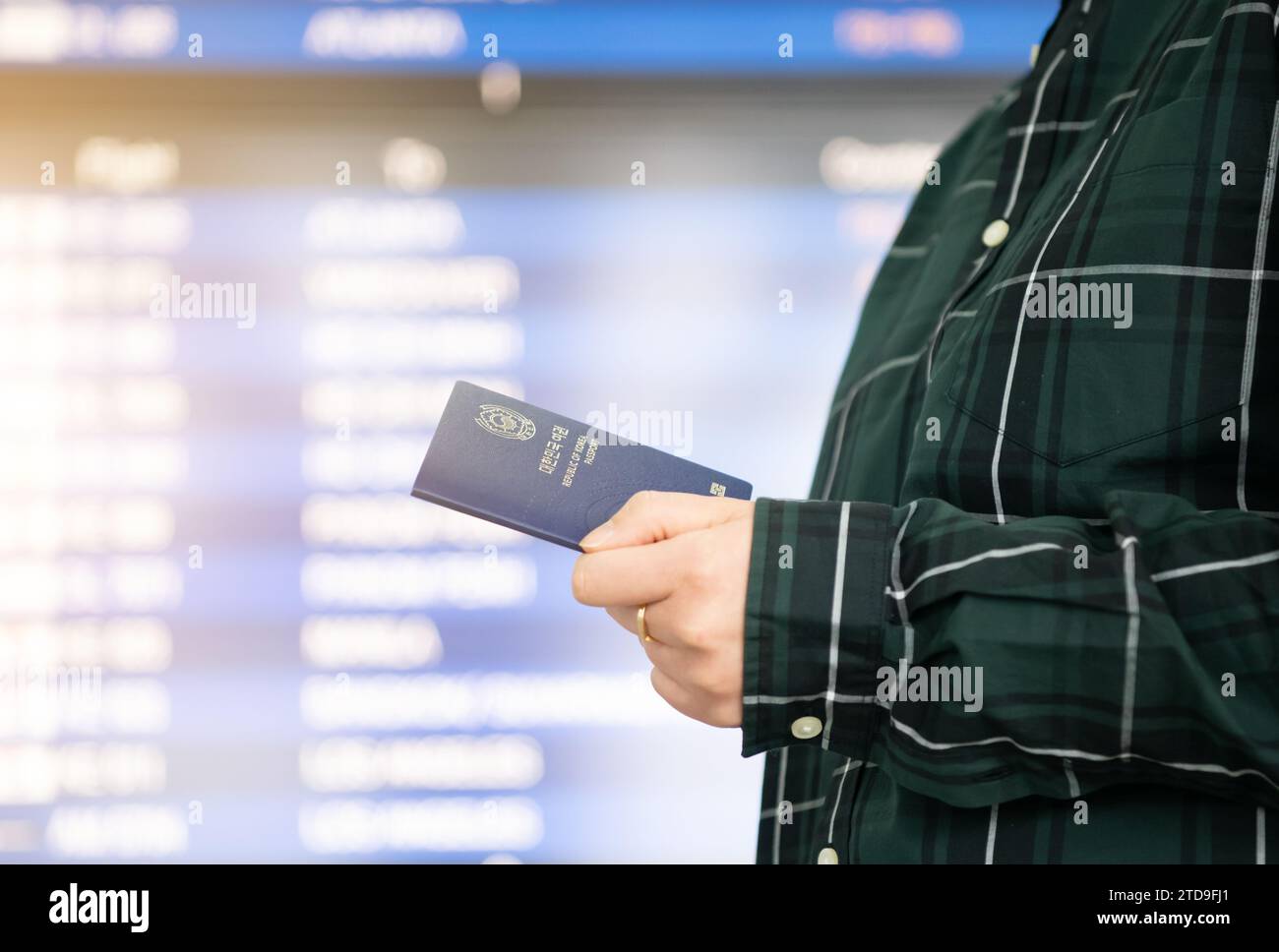 Una donna che passa di fronte a un cartello informativo sugli orari dell'aeroporto con il passaporto in mano Foto Stock