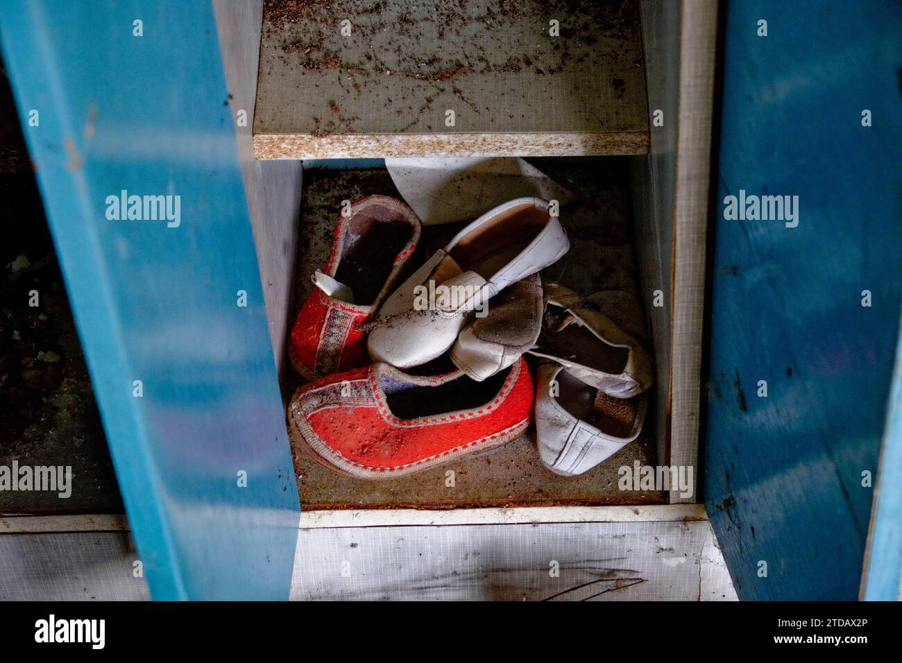Un paio di scarpe vecchie e usurate all'interno di un armadietto metallico aperto e arrugginito. Le scarpe sono rosse e bianche e l'armadietto è blu. Pantofole per bambini piccoli Foto Stock