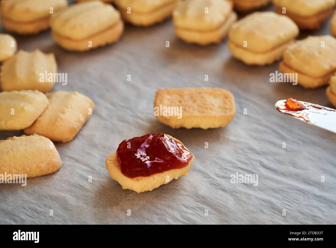 Riempire i biscotti di Natale fatti in casa con marmellata di fragole utilizzando un coltello Foto Stock