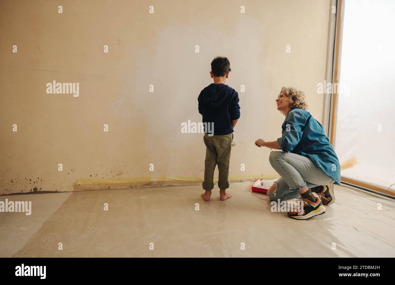 Madre di supporto che parla con suo figlio, incoraggiandolo durante la ristrutturazione della casa. Mamma e figlio dipingono le pareti interne per darti vita e colore Foto Stock