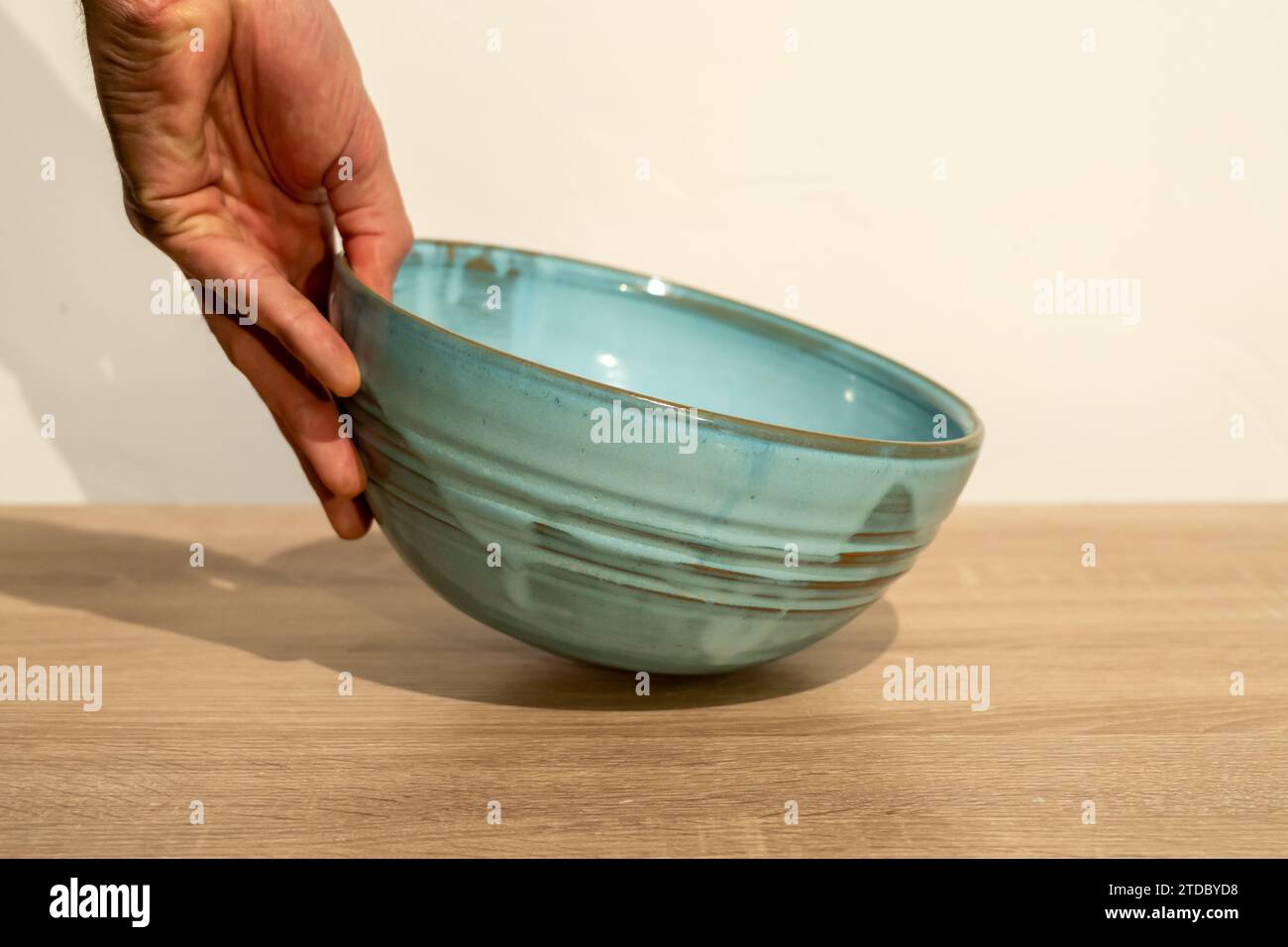 Una persona tiene una ciotola per insalata blu. Foto di alta qualità. Ceramica fatta a mano. Tavolo in legno fatto a mano. Mano umana. Fotografia del prodotto. Foto Stock