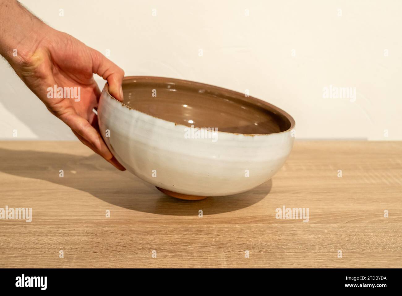 Una persona tiene una ciotola per insalata rossa e bianca. Foto di alta qualità. Ceramica fatta a mano. Tavolo in legno fatto a mano. Mano umana. Fotografia del prodotto. Foto Stock