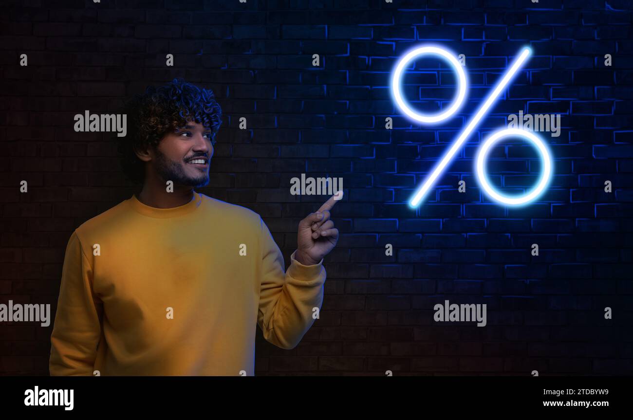 Offerta scontata. Uomo felice che indica il simbolo della percentuale di neon sul muro di mattoni al buio, design dello striscione Foto Stock
