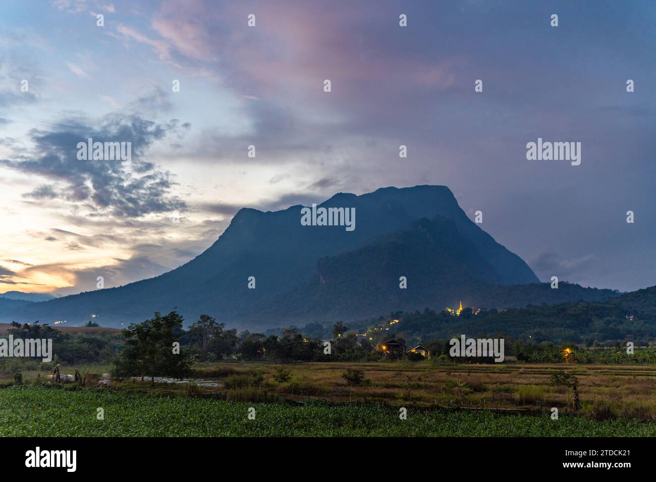 Vista di Doi Luang Chiang Dao durante un tramonto serale con un campo verde in primo piano e una spettacolare formazione di nuvole sullo sfondo Foto Stock