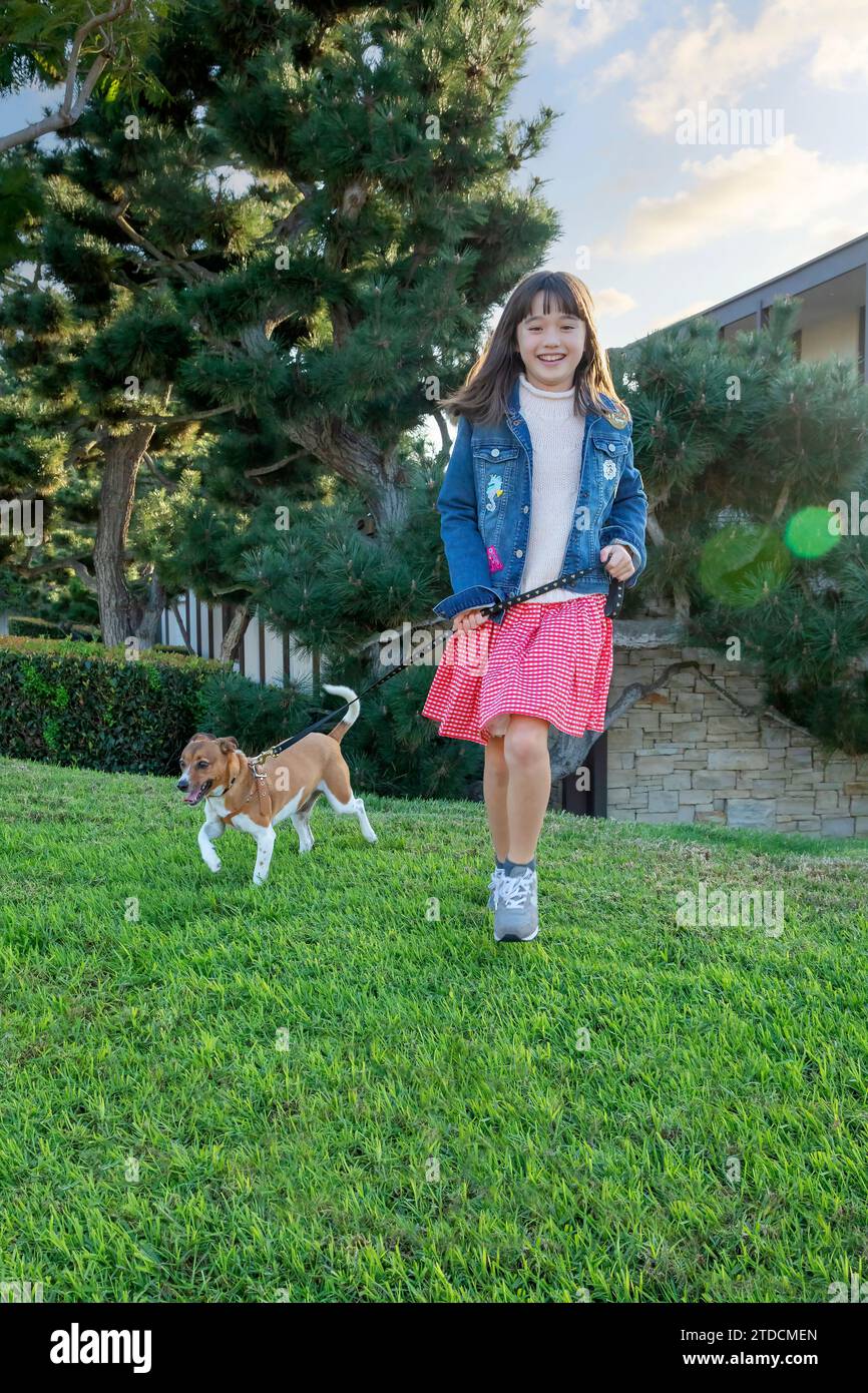 Una bambina di nove anni che corre con il suo cane in giardino Foto Stock