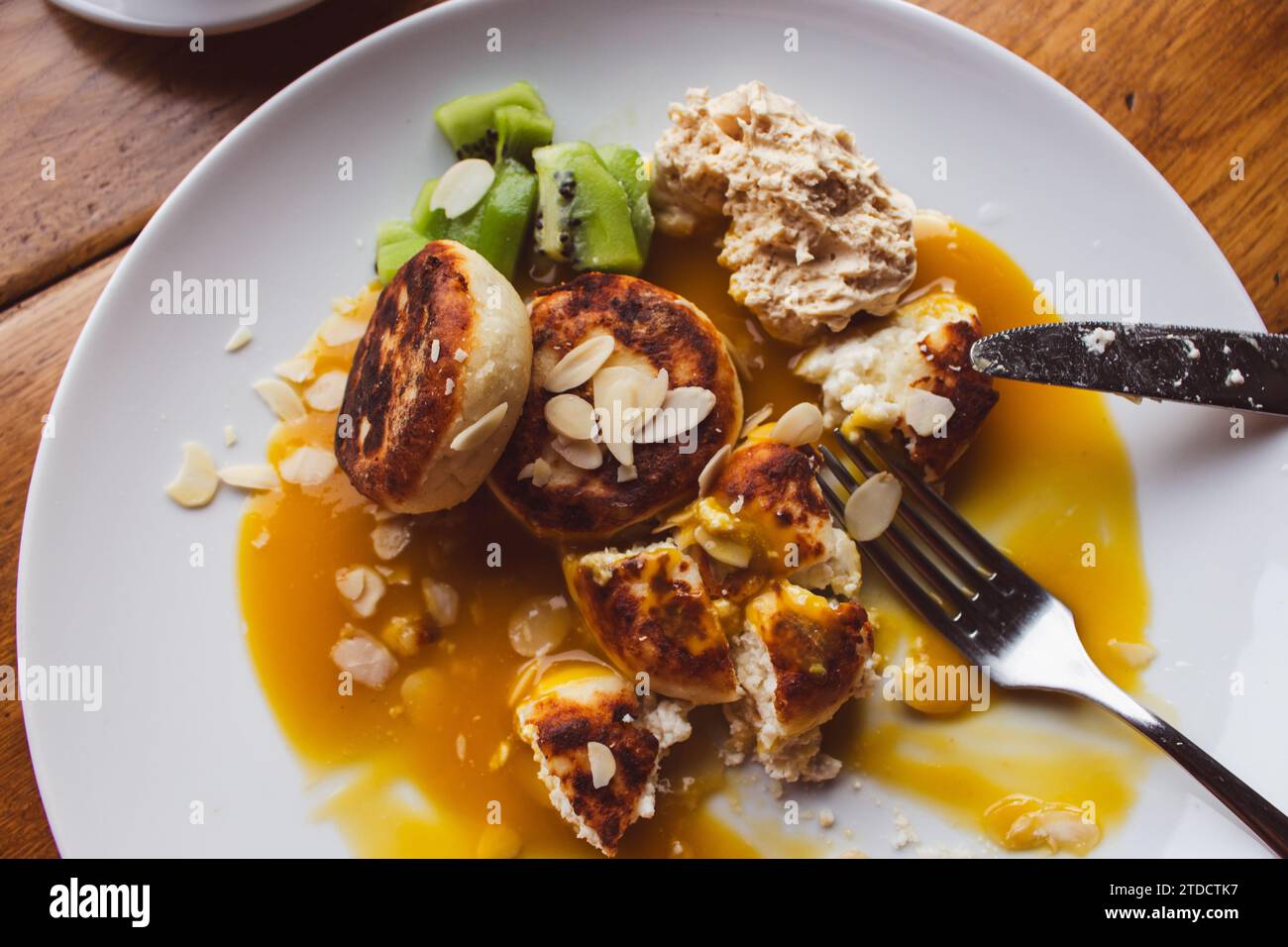 Cheesecake con sciroppo di mango e fiocchi di mandorle su piatto bianco. Colazione dolce nella caffetteria. Syrnik con cottage e avocado. Pancake al formaggio con sciroppo. Foto Stock