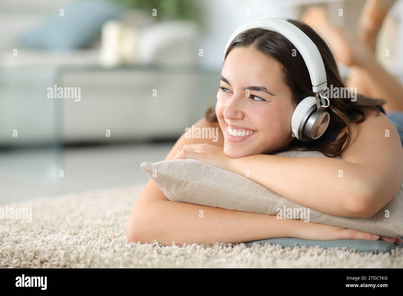 Donna felice che ascolta musica con le cuffie sdraiate su un tappeto a casa Foto Stock