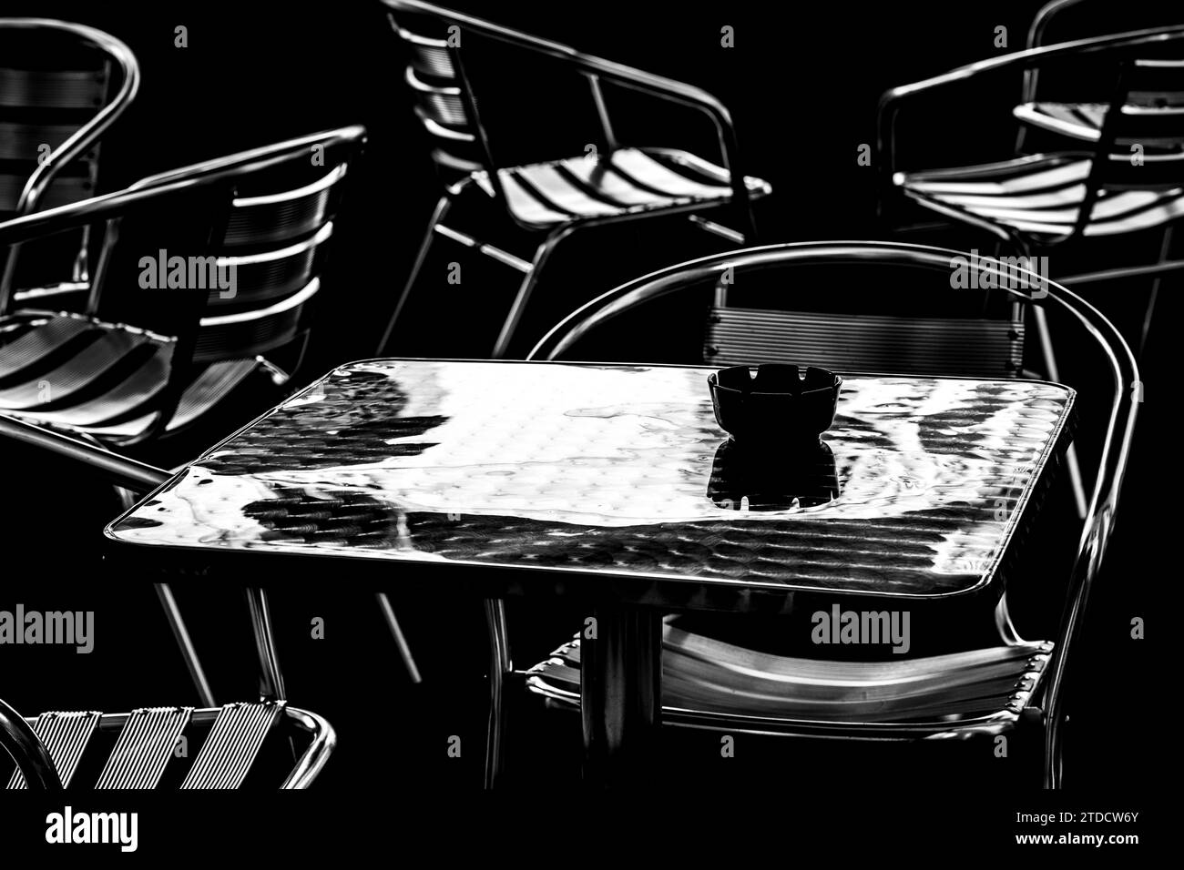 Immagine minimale in bianco e nero di un tavolo in metallo circondato da sedie. Posacenere nero su una superficie in alluminio. Foto Stock