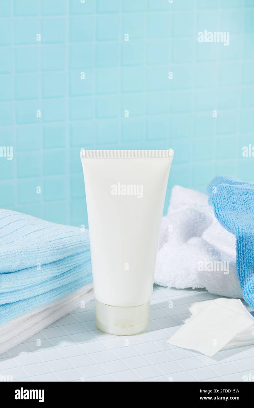 Primo piano di un tubo di detergente per il viso con asciugamani e coppette di cotone su sfondo blu e bianco. Concetto di cosmetici per la pulizia della pelle. Foto Stock