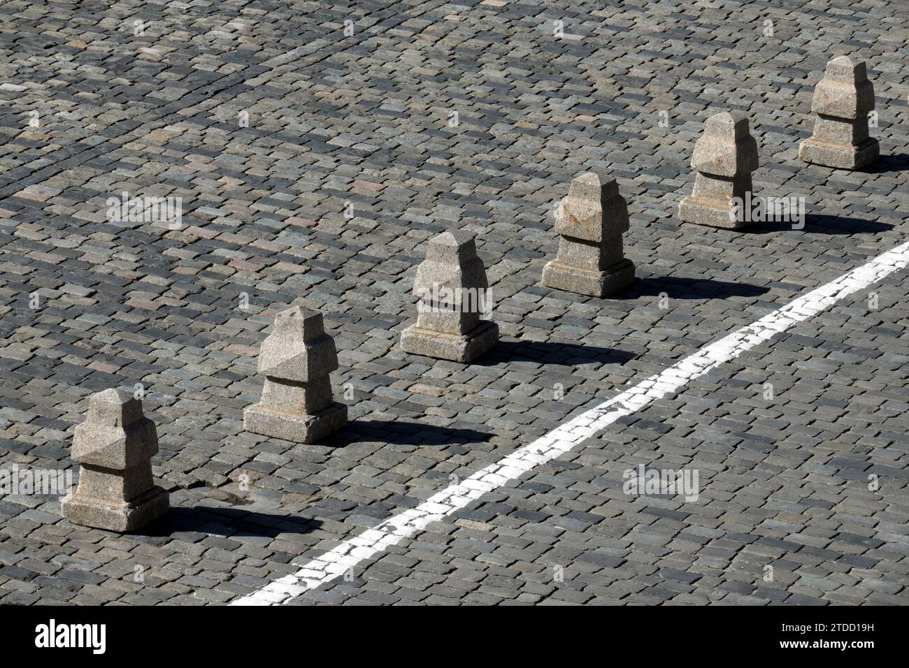 Barriera dalle piramidi di granito dopo una lunga linea bianca sulla vista laterale della pavimentazione stradale in pietra Foto Stock