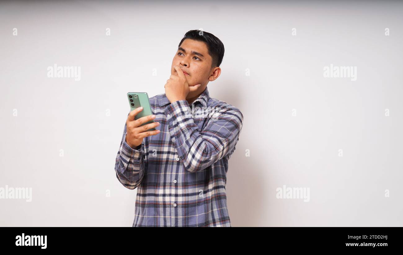 Giovane asiatico che tiene il suo telefono cellulare con un'espressione triste e confusa su sfondo bianco. foto studio Foto Stock