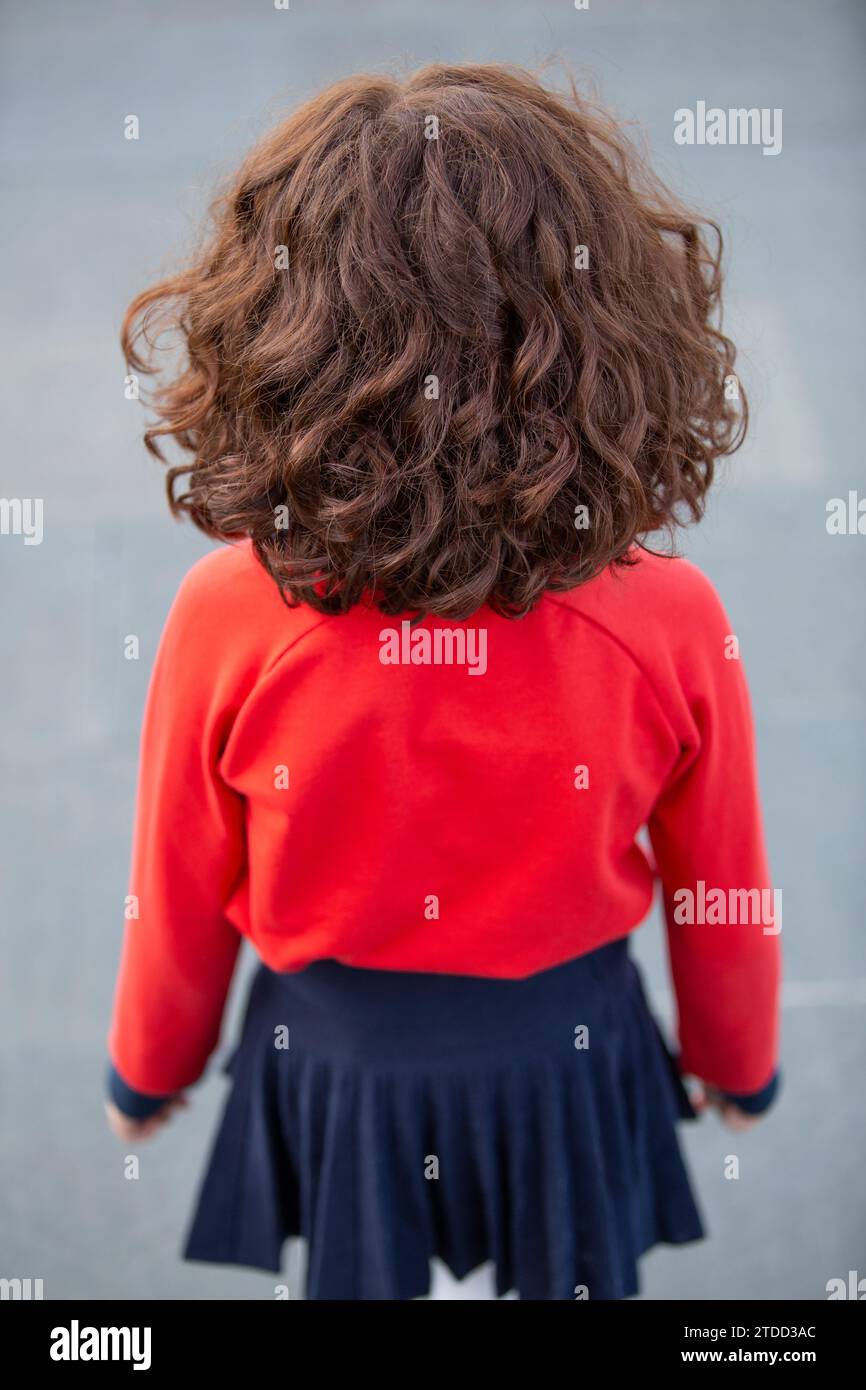 Vista posteriore di una ragazza con un ponticello rosso in piedi all'aperto Foto Stock