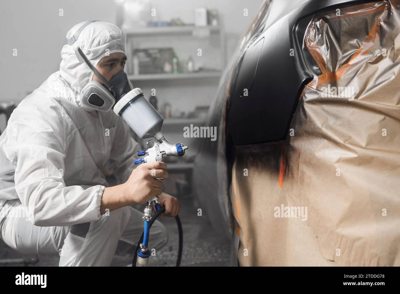 Uomo verniciatore a spruzzo che dipinge la carrozzeria dell'auto nella cabina di verniciatura. Foto Stock