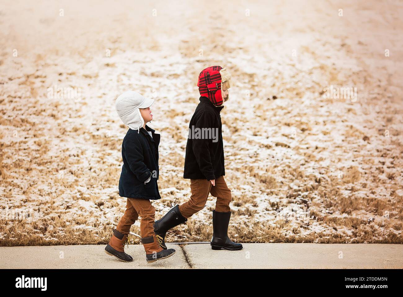 due ragazzini che camminano indossando cappelli e stivali con la neve dietro di loro Foto Stock