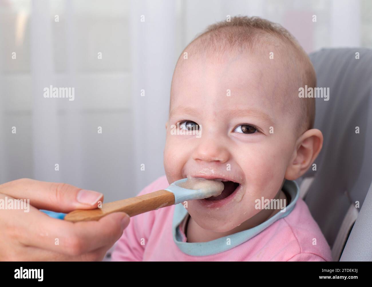 La mano della madre dà da mangiare al porridge di grano saraceno. Il bambino sorridente ride e guarda la telecamera. Spazio di copia per il testo Foto Stock