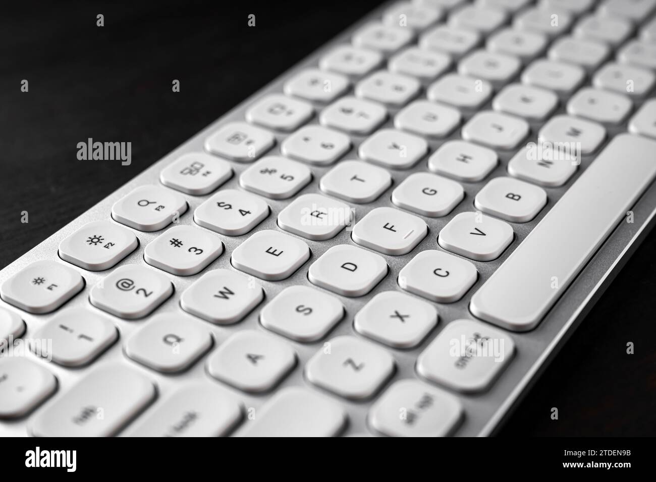 Tastiera per computer in alluminio bianco su scrivania da ufficio in legno scuro, messa a fuoco selettiva Foto Stock