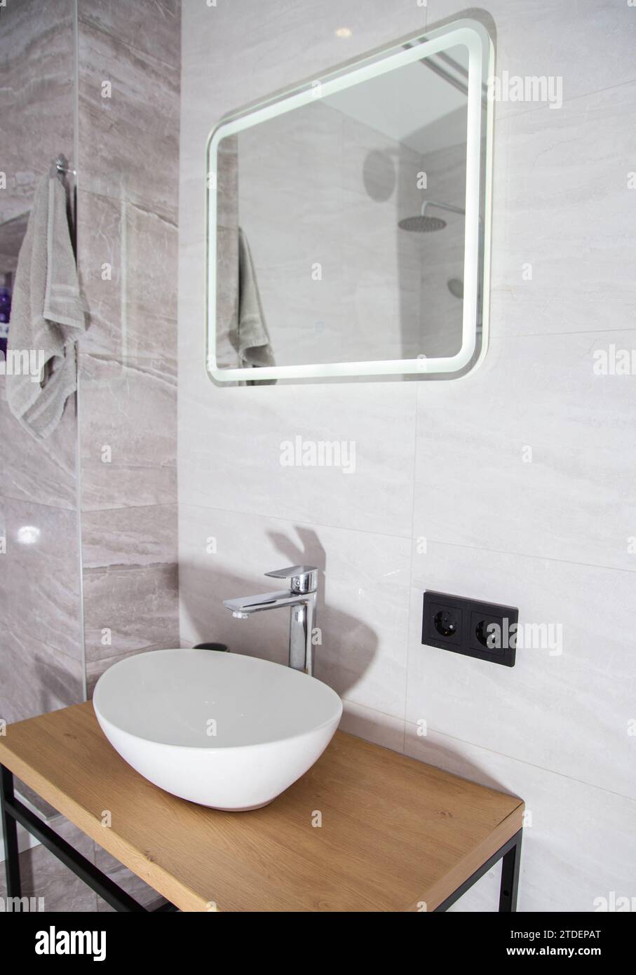 Moderno interno del bagno, specchio con illuminazione a LED e lavabo con ripiano in legno. Foto Stock