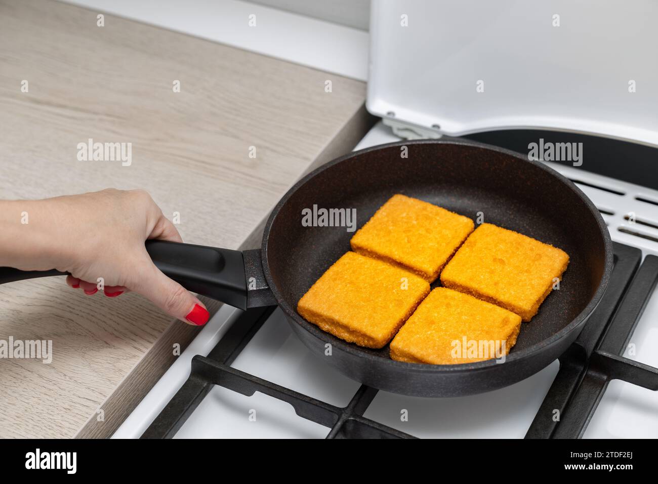 donna che frigge cotolette di pesce impanate in una padella. fare grandi pepite a casa. cotoletta impanata Foto Stock