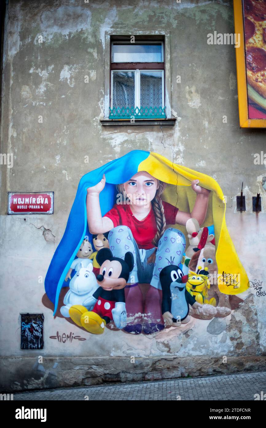 Un murale di una giovane ragazza che si rifugia sotto una bandiera Ucraina a Praga. Street art murale di ChemiS Foto Stock