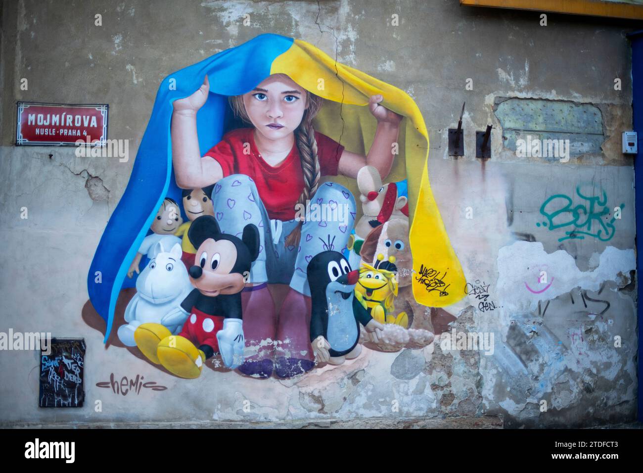 Un murale di una giovane ragazza che si rifugia sotto una bandiera Ucraina a Praga. Street art murale di ChemiS Foto Stock