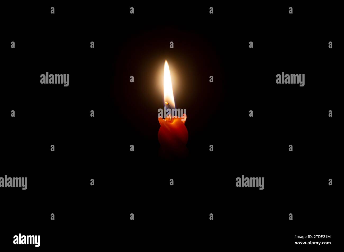 Una sola candela accesa o una luce si accende su una candela arancione su sfondo nero o scuro sul tavolo della chiesa per Natale, funerale Foto Stock