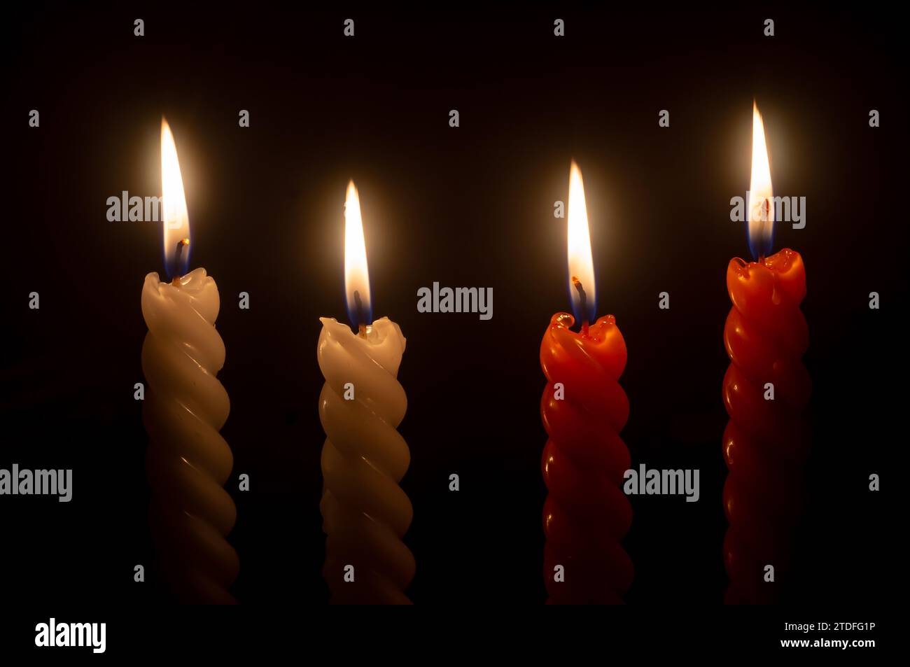 La fiamma o la luce della candela in fiamme si accendono su quattro candele a spirale su sfondo nero o scuro sul tavolo della chiesa per Natale, funerale o memoriale Foto Stock