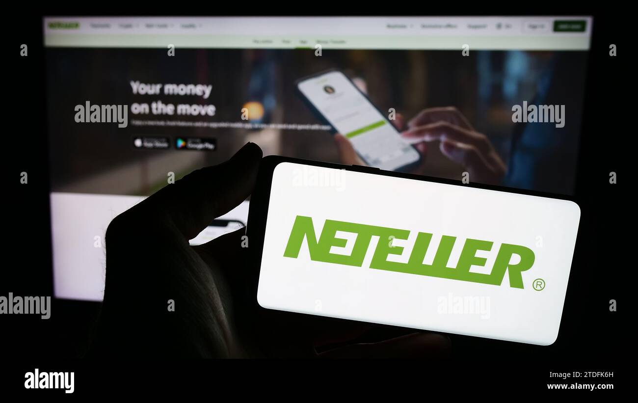 Persona che possiede uno smartphone con il logo della società Neteller, una piattaforma di pagamenti globale, davanti al sito Web. Concentrarsi sul display del telefono. Foto Stock