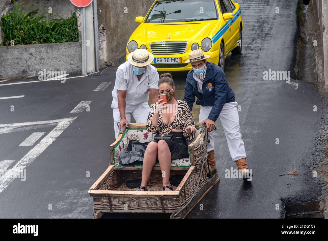FUNCHAL, PORTOGALLO - 24 AGOSTO 2021: Una donna non identificata rotola per la strada in cesti di vimini (toboga) con l'aiuto di conducenti tradizionali Foto Stock