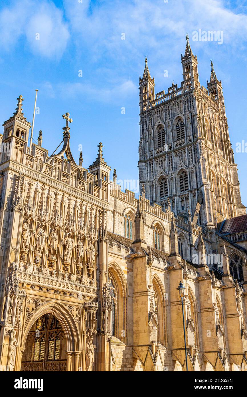 Luce del sole del mattino sul portico splendidamente intagliato e la torre decorata del XV secolo della Cattedrale di Gloucester, Gloucester UK vista contro un blu sk Foto Stock