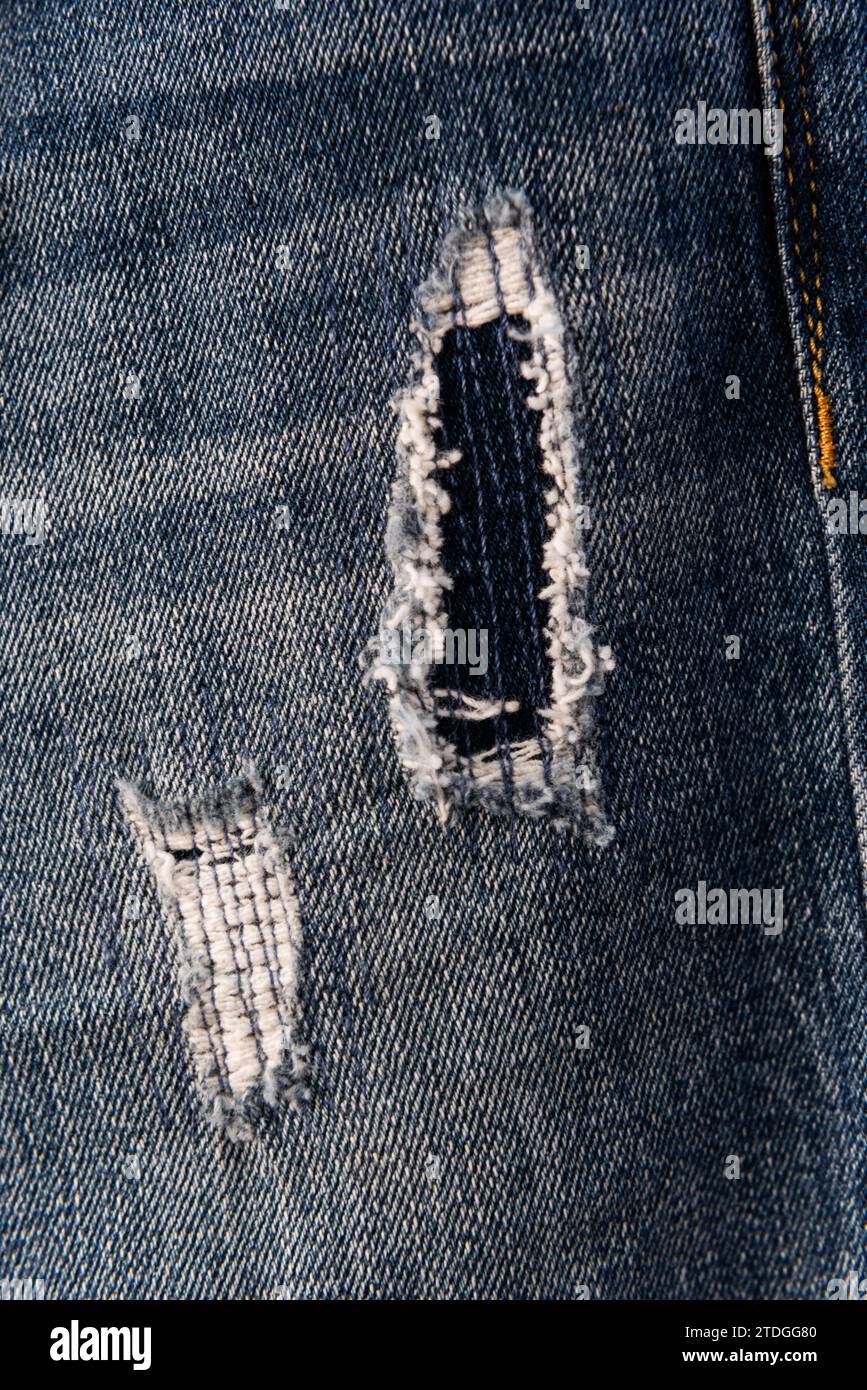 Primo piano di un paio di pantaloni jean in denim blu lacerato, strappato e sfilacciato con fori e fili allentati. Foto Stock