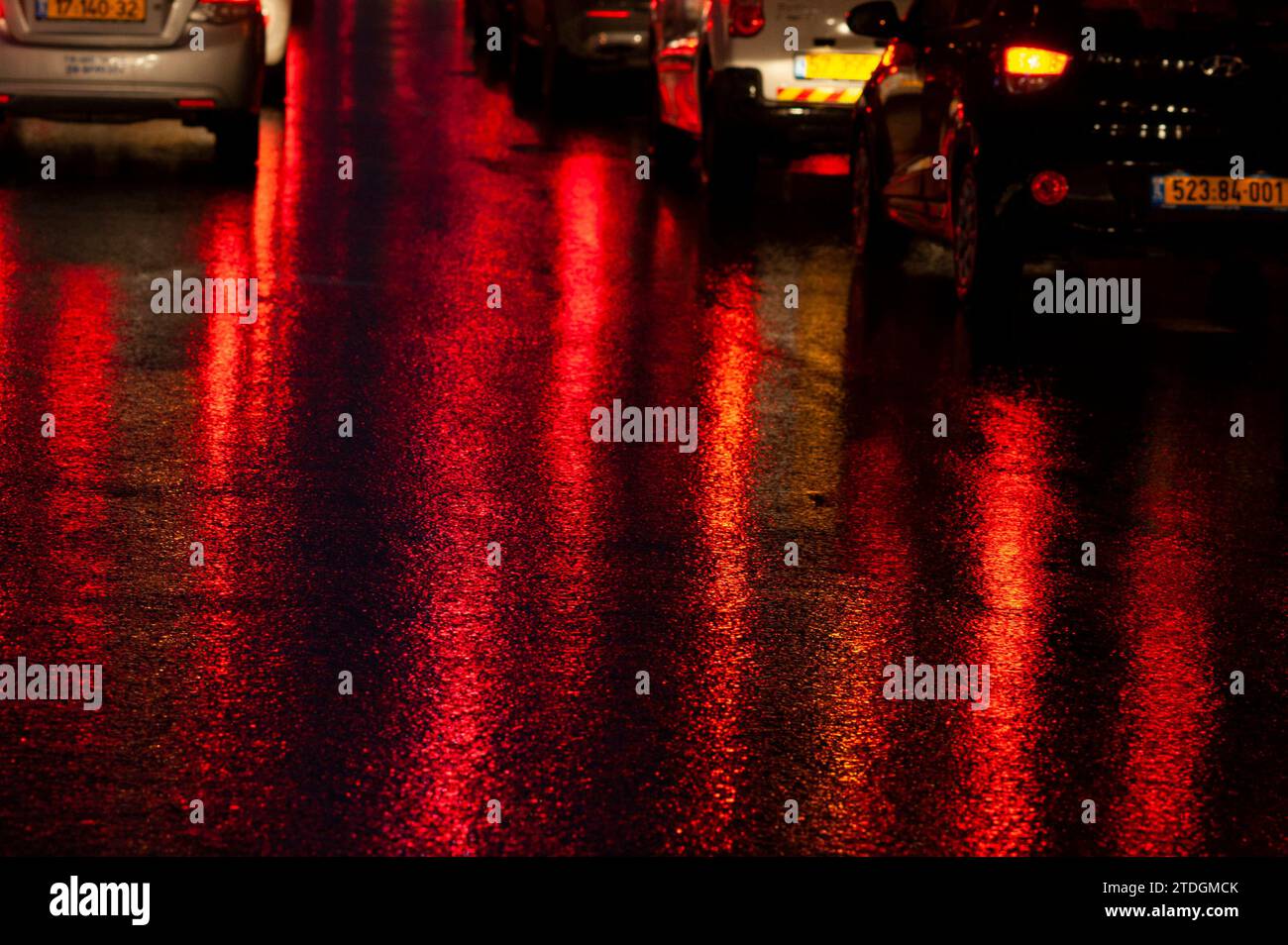 Strada asfaltata bagnata e astratta, colorata di notte da luci di posizione posteriori rosse e semafori. Foto Stock