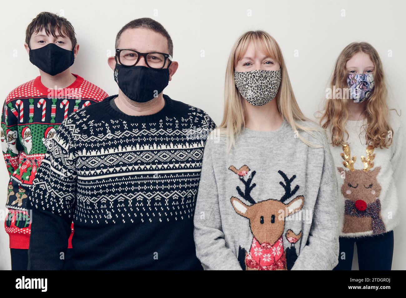 Una famiglia scatta una foto Covid Christmas Family con maglioni di Natale e maschere facciali, su sfondo bianco. Foto Stock