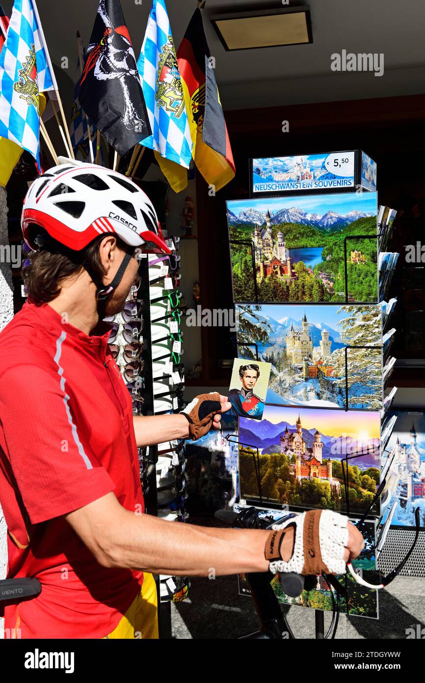 Ciclista che guarda le cartoline kitsch di fronte al castello di Hohenschwangau, alta Baviera, Baviera, Germania Foto Stock